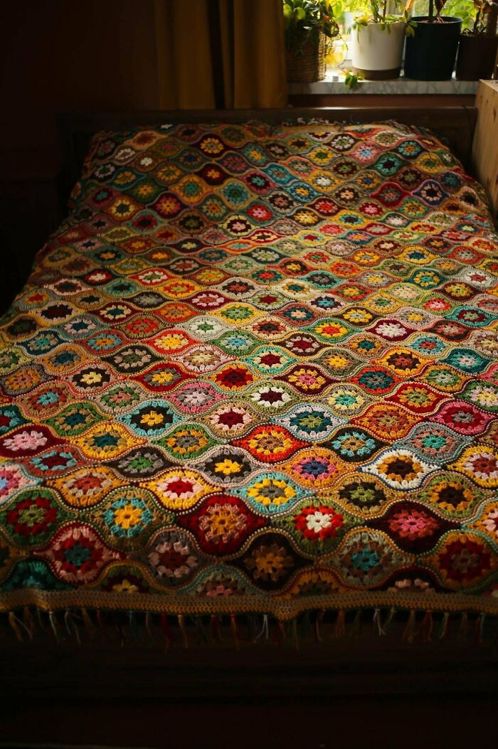 Colorful crocheted blanket with intricate patterns displayed on a bed.