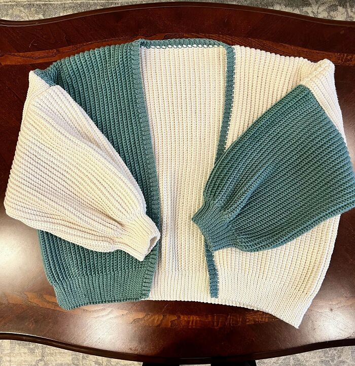 Chunky green and white crochet cardigan with balloon sleeves displayed on a wooden surface by crochet enthusiasts.