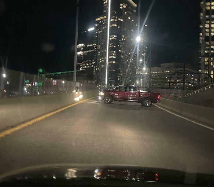 Red pickup truck blocking a city highway lane at night, showcasing drivers' poor judgment in challenging situations.