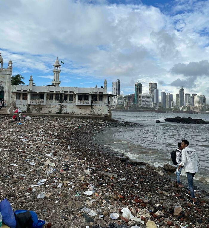 Urban hellscape showing a polluted shoreline with litter, an old building, and a distant city skyline.