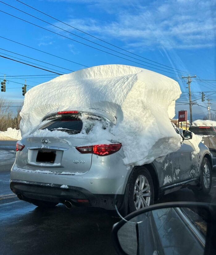 Car covered in a thick layer of snow, driving on a street, illustrating risky driving behavior.