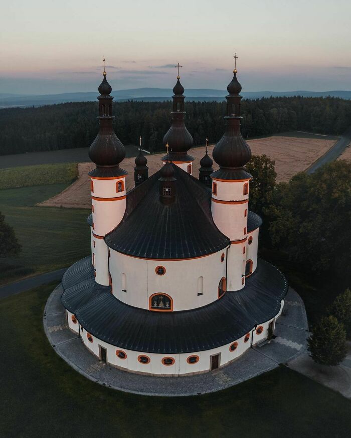 Aerial view of a fascinating church surrounded by trees and fields at sunset.