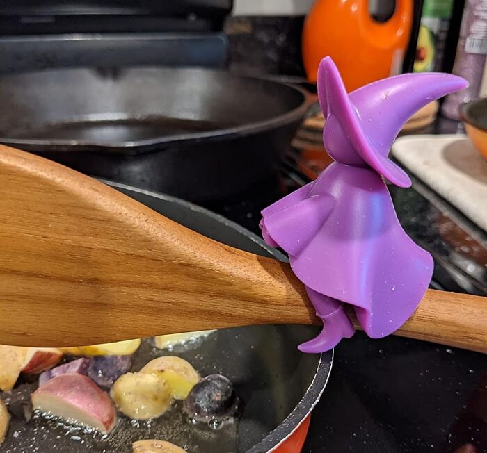 Weird kitchen item: a purple witch-shaped spoon holder on a wooden spoon over a cooking pot.
