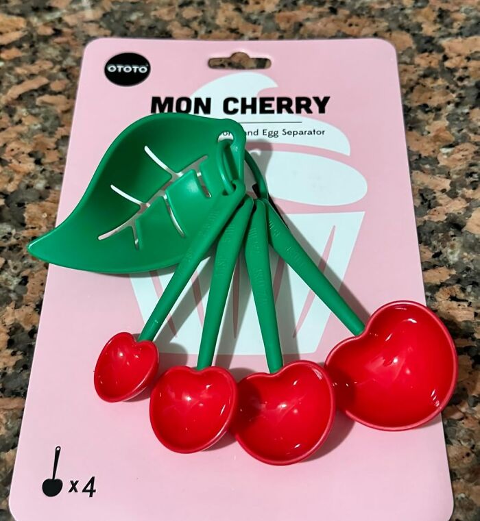 Cherry-shaped measuring spoons and egg separator on a pink card, showcasing unusual kitchen items.