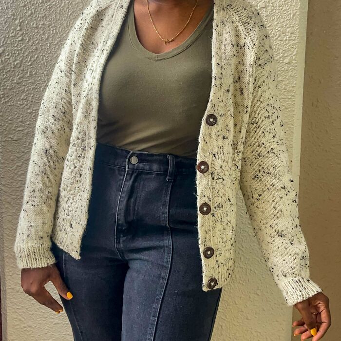 Woman wearing a handmade crochet cardigan with buttons, paired with a green top and high-waisted dark jeans.