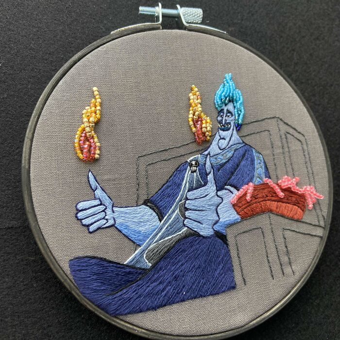 Embroidery design of a blue character with flaming hair giving thumbs up, featuring detailed colorful stitch work.