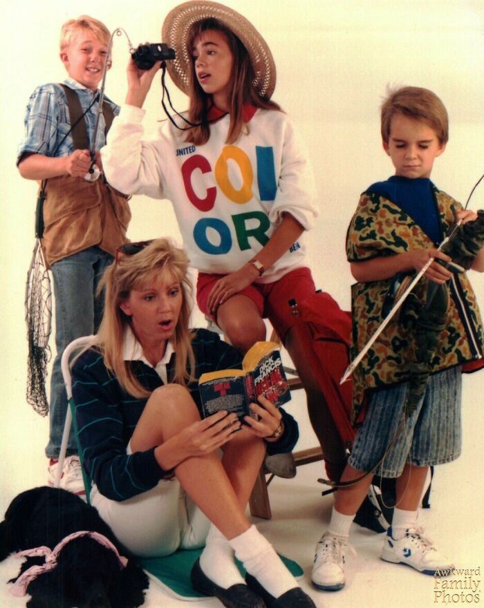 Family shares awkward family photo with kids dressed in vintage outdoorsy costumes and a mother reading a book nearby.