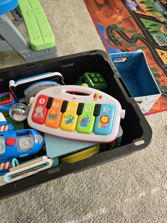 Colorful children's toys in a box on a carpet, including a musical toy with numbers and animal images.