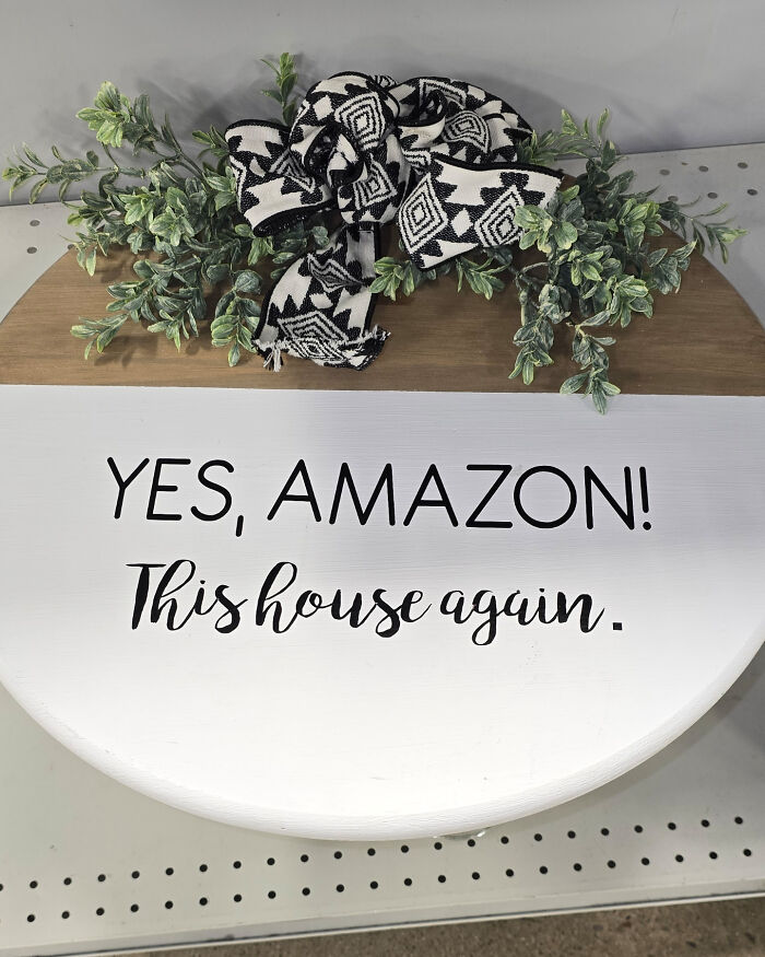 Decorative sign with "YES, AMAZON! This house again," humorously expressing consumerism fatigue.