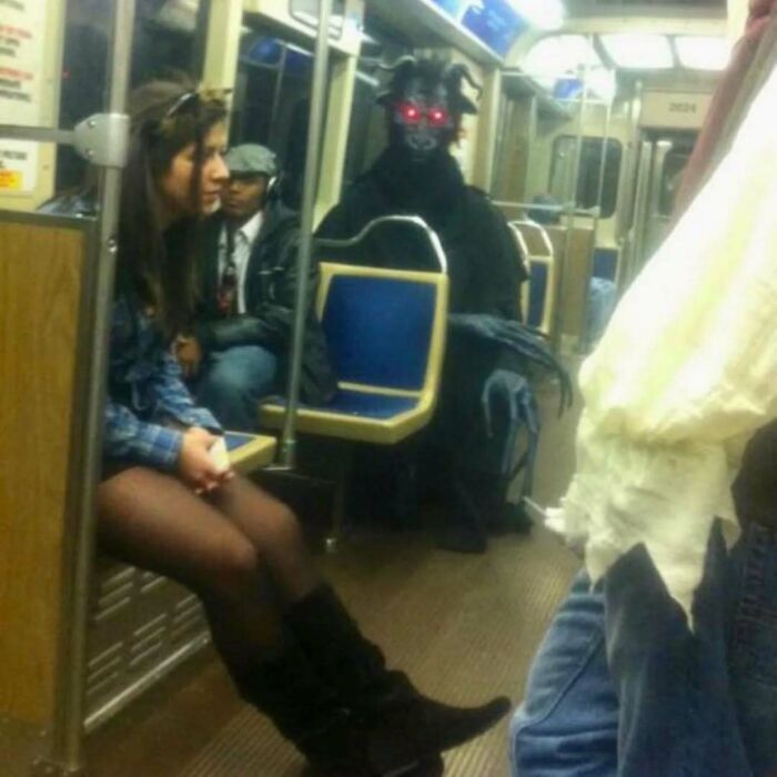 Passenger sitting on public transit near a person in a dark costume with glowing red eyes, a random photo for processing.