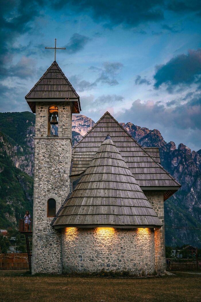 Stone church with wooden roof and bell tower against mountain backdrop, showcasing fascinating church architecture.