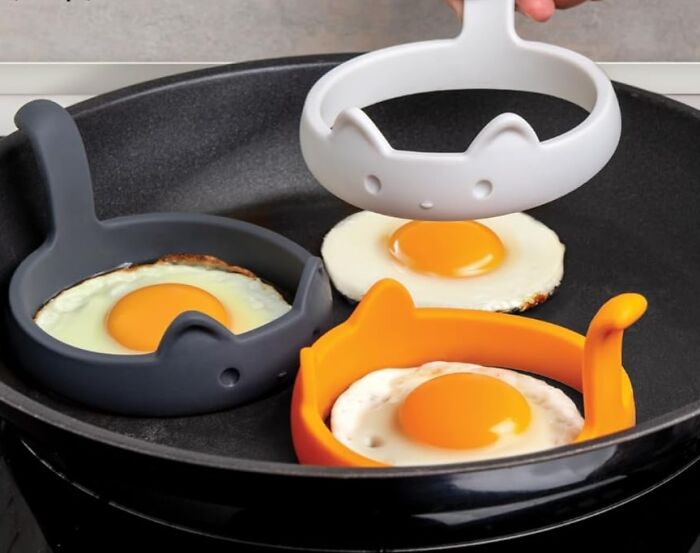 Silicone egg molds shaped like animals cooking sunny side up eggs in a frying pan, showcasing fun and functional kitchen tools.