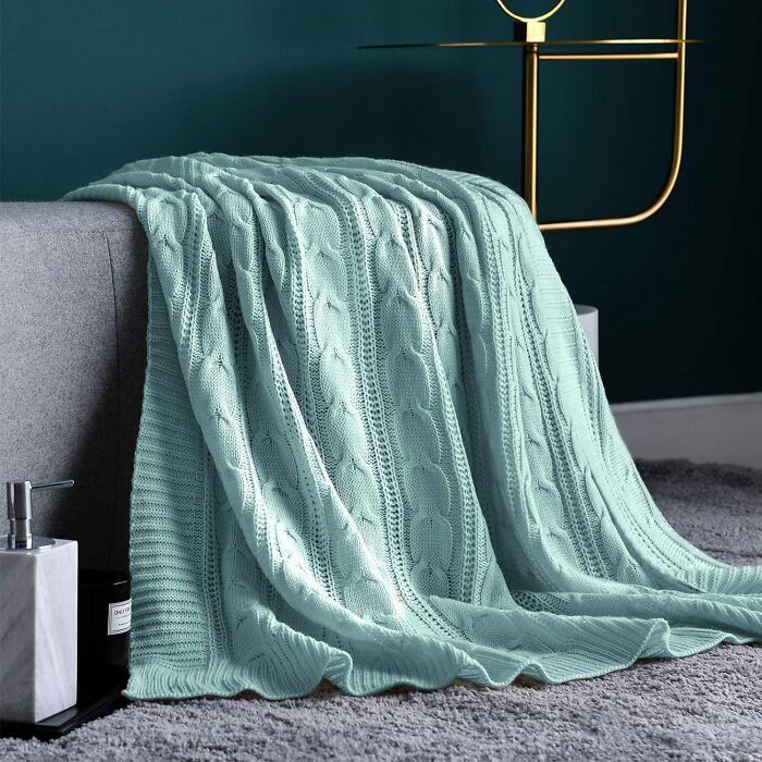Mint green cozy blanket draped over a gray sofa in a stylish living room.