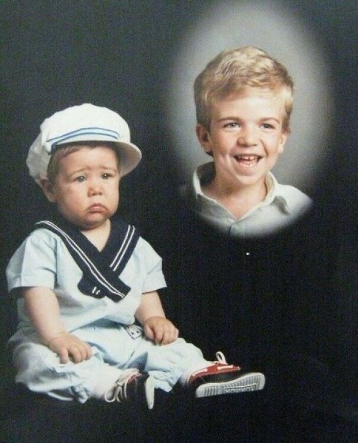 Two young siblings in an awkward family photo, one in a sailor outfit looking sad, the other smiling warmly nearby.