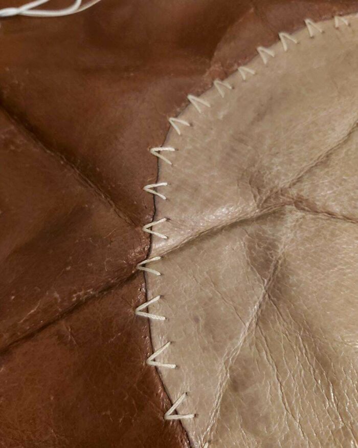 Close-up of a patchwork leather piece stitched with white thread, representing ironic consumerism.