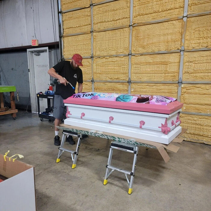 Man painting pink and white casket with TikTok design, showcasing fascinating creativity in a garage setting.
