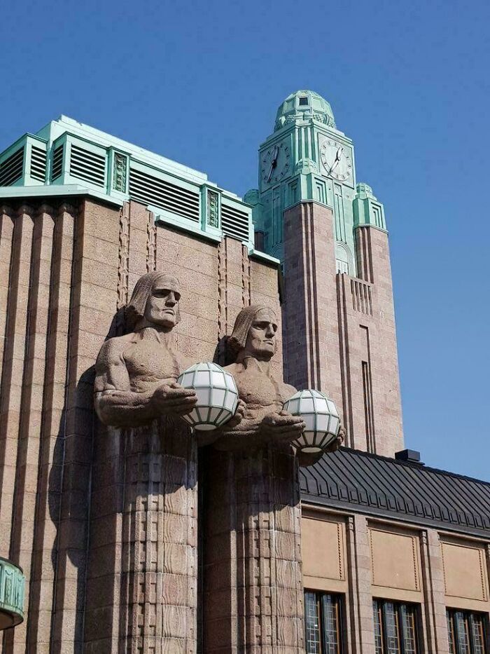 Art deco architectural feat with large statues holding spherical lamps on a historic building under clear blue sky.