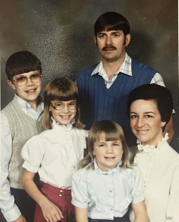 Vintage awkward family photo featuring parents and three children with retro hairstyles and glasses, evoking sweet nostalgia.