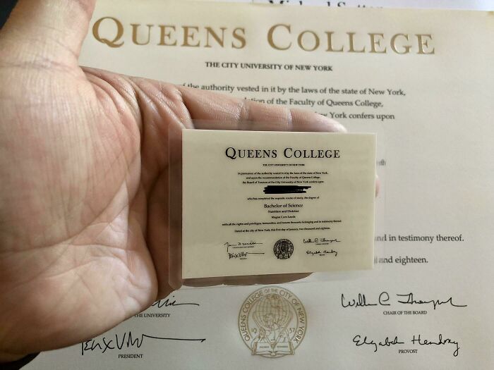 A hand holding a miniature Queens College diploma, showcasing cool products with surprises.