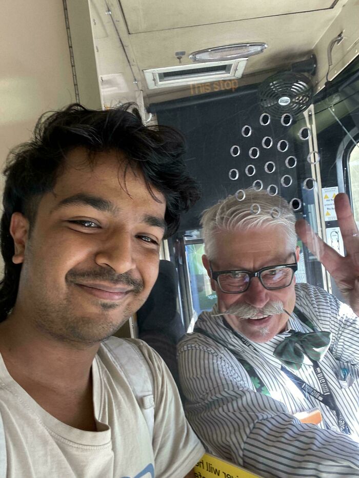Two men in an Australian bus, one making a peace sign through a glass divider, sharing a moment.