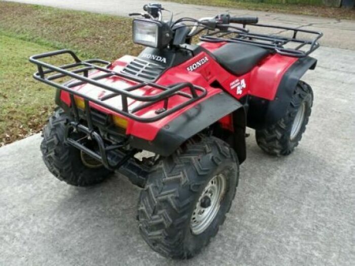Red 80s nostalgia Honda ATV with large tires, parked on concrete.
