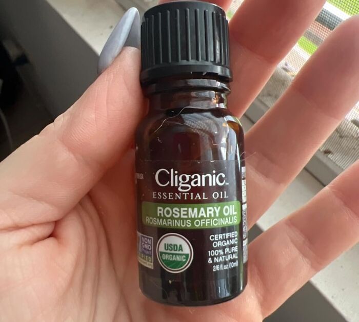 Hand holding a bottle of Cliganic rosemary essential oil, a treasure to reward yourself.