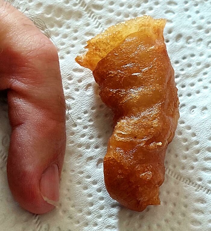 Golden-brown fried object resembling a finger, showcasing pareidolia on a paper towel next to a human thumb.