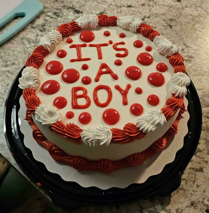 Funny wholesome cake with red icing and white swirls, displaying the message "It's a boy" in red letters.