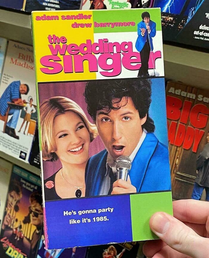 Hand holding a VHS of "The Wedding Singer," featuring a 90s retro design and famous actors on the cover.