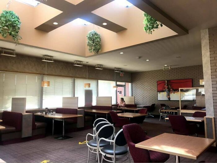 A nostalgic '90s diner interior with skylights and hanging plants, featuring maroon booths and empty seating.