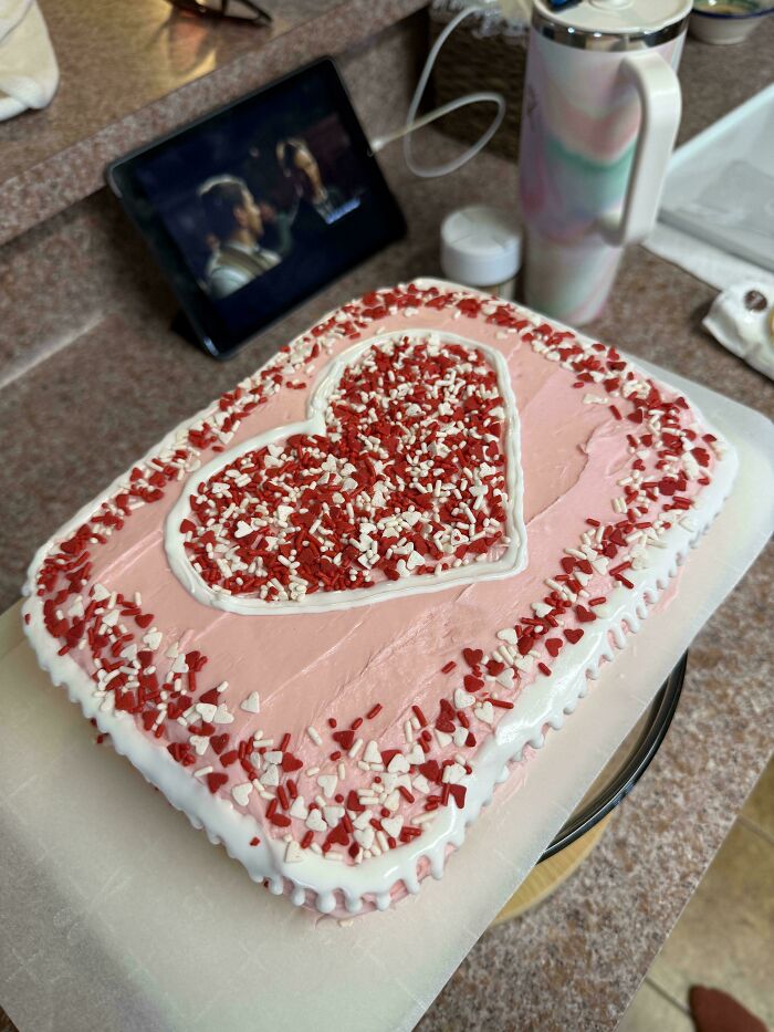A heart-shaped cake with pink frosting and red, white sprinkles, showcasing an elevated baking creation.