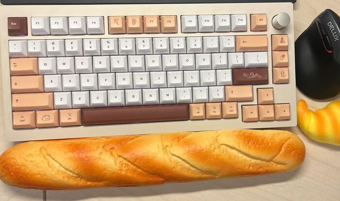 Mechanical keyboard with unique pastel keycaps and novelty bread wrist rest enhancing desk joy during workdays.
