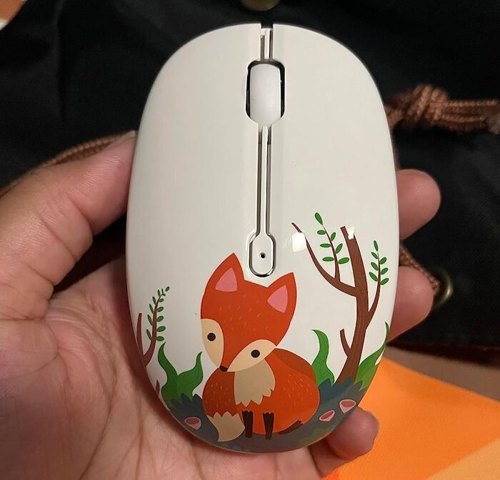Hand holding a computer mouse featuring a cute fox illustration, one of the desk joy items to improve workday experience.
