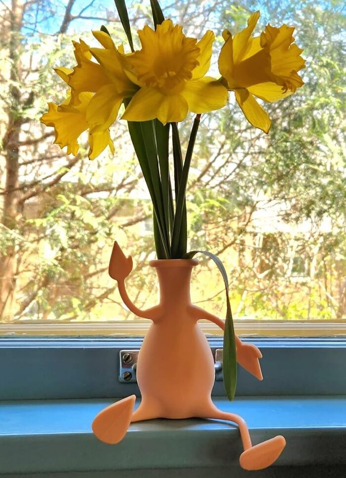 Playful flower vase holding yellow daffodils on a window sill, a cheerful desk joy item to brighten your workday.