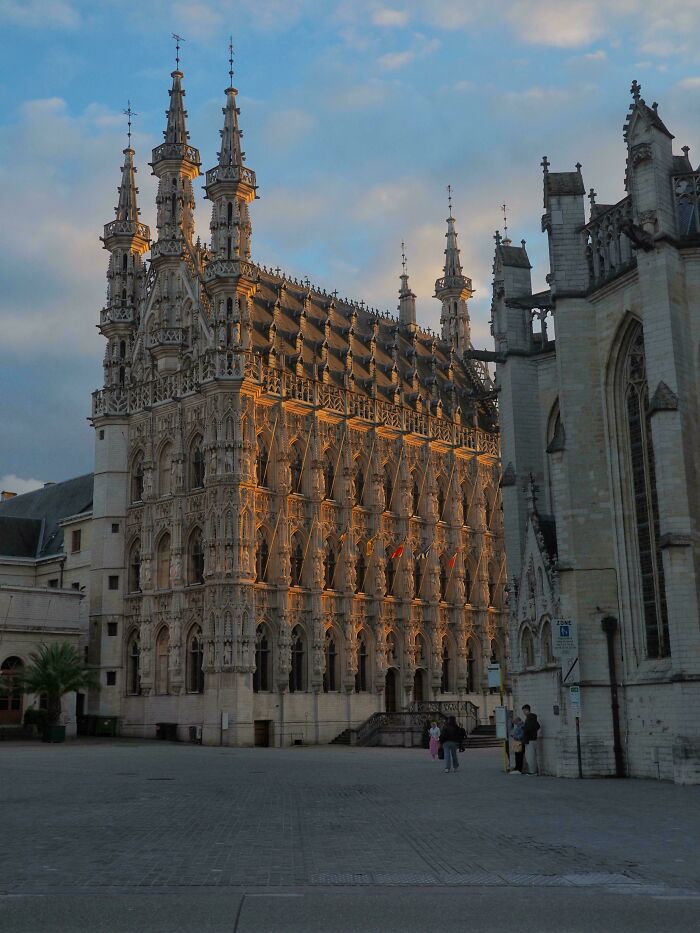 Gothic architectural feat with detailed stone carvings and spires illuminated by evening light in a historic town square.