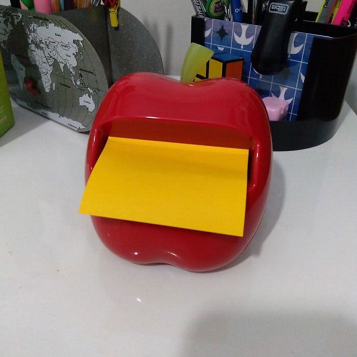 Red apple-shaped sticky note dispenser on a desk, illustrating fun office supplies.