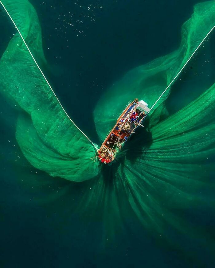Aerial view of a fishing boat surrounded by scarily big green fishing nets on dark ocean water for megalophobia.