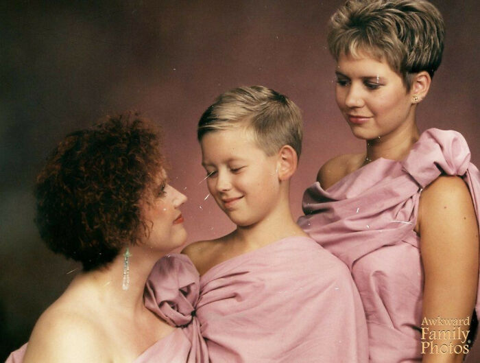 Three family members in matching pink fabric smiles awkwardly in a sweet and awkward family photo portrait.
