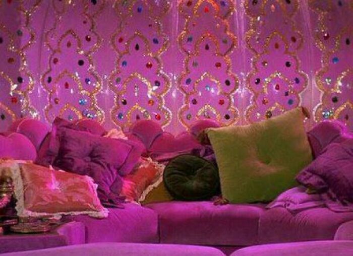 Velvet vintage couch with decorative pillows and purple wallpaper featuring intricate nostalgic patterns.