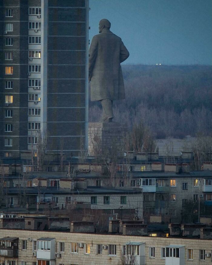 Massive statue towering over gloomy Soviet-era buildings with a dark, evil aura resembling a supervillain headquarters.