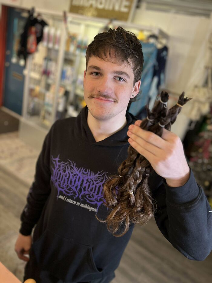 Young man with fierceflow beautiful hair men style holding cut braided hair indoors, smiling at the camera.