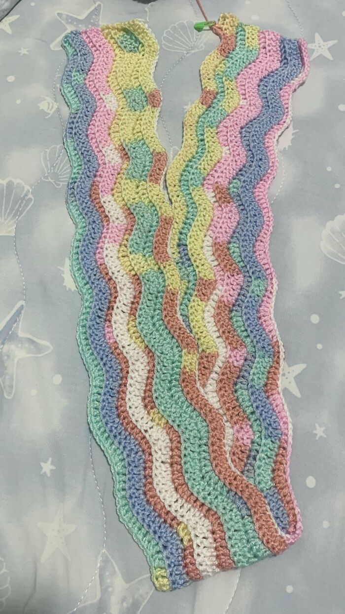 Crochet enthusiasts proud of colorful wavy striped crochet project in pastel colors on a starfish patterned background.