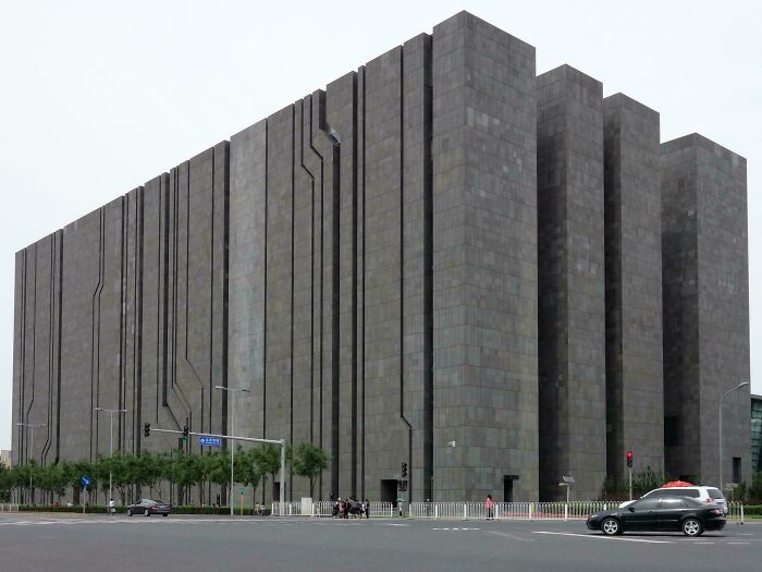 Massive gray building with dark lines, exuding an evil aura, resembling a supervillain headquarters in an urban setting.