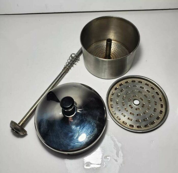Vintage stainless steel coffee percolator parts disassembled on a white surface in a nostalgic photo.