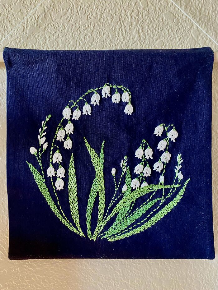 Embroidery design of white bell-shaped flowers with green stems on a dark blue fabric background.