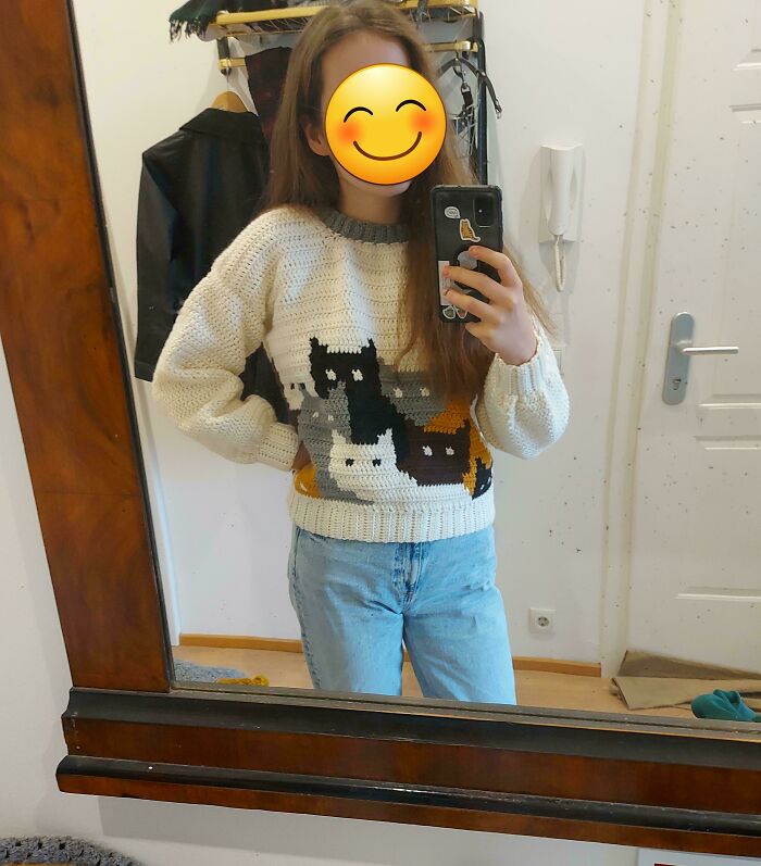 Person taking a mirror selfie wearing a crocheted sweater with cat designs, showcasing proud crochet project.