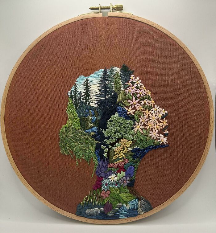 Embroidery hoop with a colorful floral and nature-inspired embroidery silhouette on brown fabric background.
