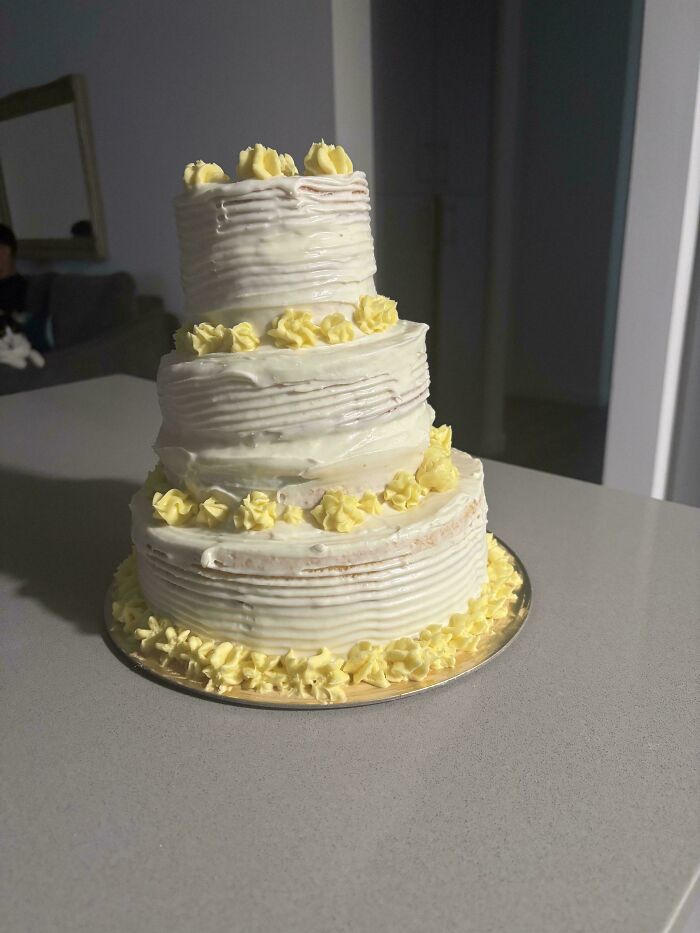 Tiered cake with white frosting and yellow decorations, showcasing a baker's culinary level-up.