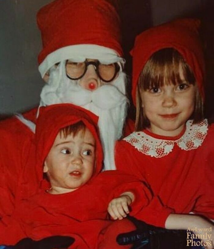 Child looking uneasy next to a girl and a person dressed as Santa Claus in an awkward family photo moment.