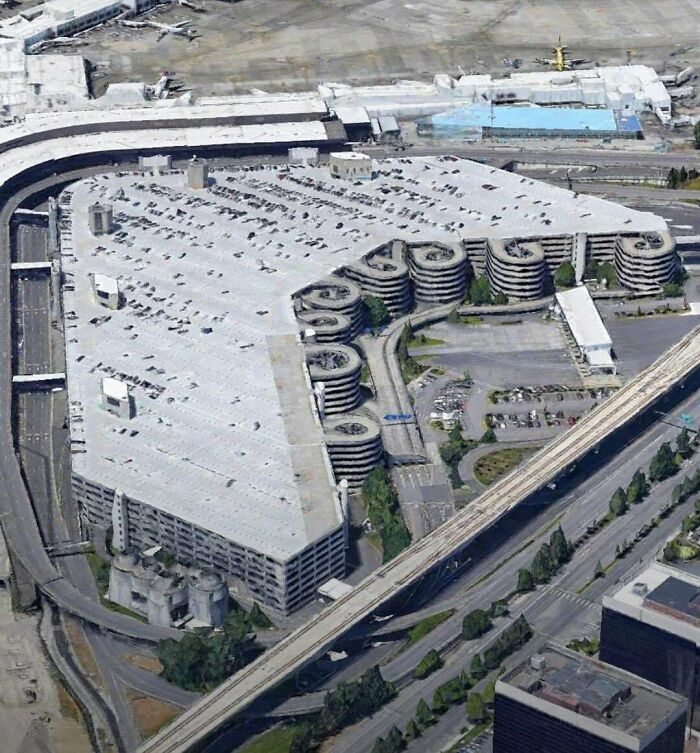 Aerial view of sprawling urban infrastructure with intertwining roads and parking structures, evoking an 'urban hell' feel.
